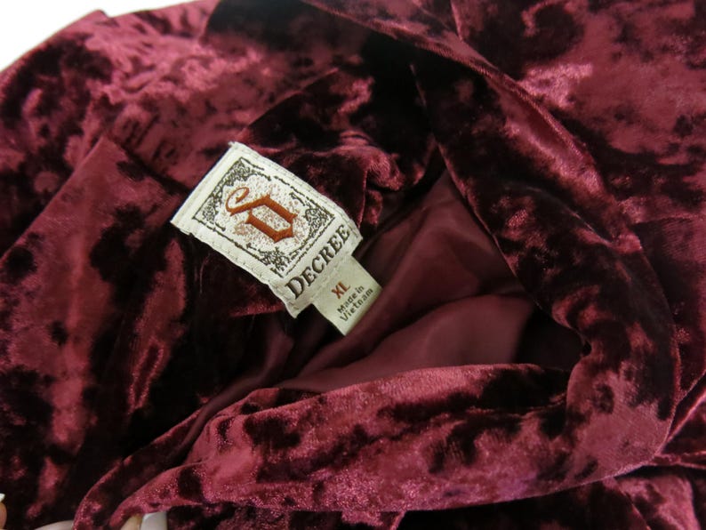 May include: A burgundy velvet robe with a large "DECREE" label, featuring a stylised "D" logo and the size "XL". Made in Vietnam.