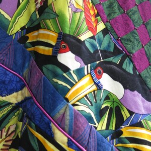 May include: A colorful fabric with a tropical print featuring toucans, leaves, and flowers. The fabric is made up of different patchwork pieces, including a purple and green checkered pattern.