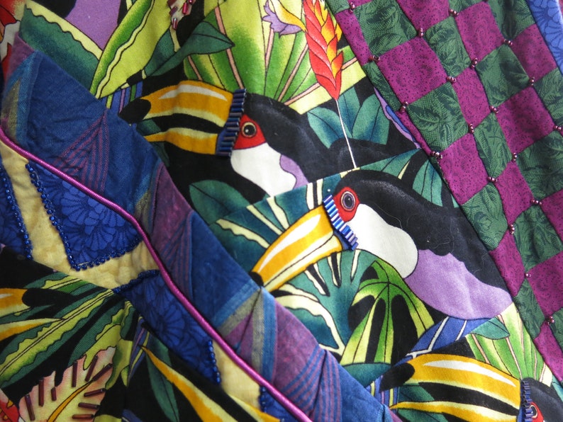 May include: A colorful fabric with a tropical print featuring toucans, leaves, and flowers. The fabric is made up of different patchwork pieces, including a purple and green checkered pattern.
