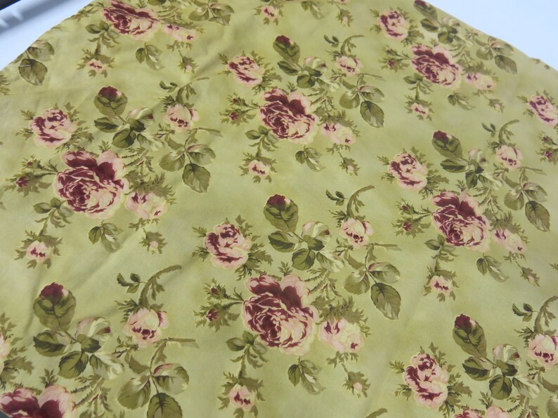 May include: A green fabric with a floral pattern featuring pink and burgundy roses. The fabric has a subtle sheen and a soft texture.