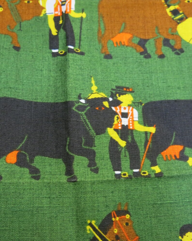 Op de afbeelding: Een groene stof met een herhalend patroon van zwarte en bruine koeien, een man in traditionele kleding en een paard. De man houdt een stok vast en het paard draagt een rood hoofdstel.