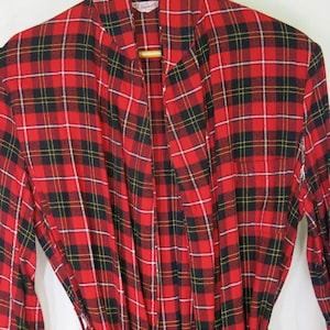 May include: A red, black, and yellow plaid robe with a matching belt. The robe is made of a soft fabric and has a shawl collar. The robe is hanging on a wooden hanger.