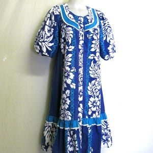 May include: A blue and white floral print dress with short sleeves and a ruffled hem. The dress features a scoop neckline with a contrasting blue trim. The fabric is patterned with white hibiscus flowers and leaves.