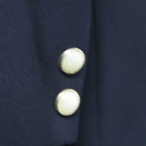 May include: Close-up of a navy blue jacket with two white pearl buttons on the sleeve.