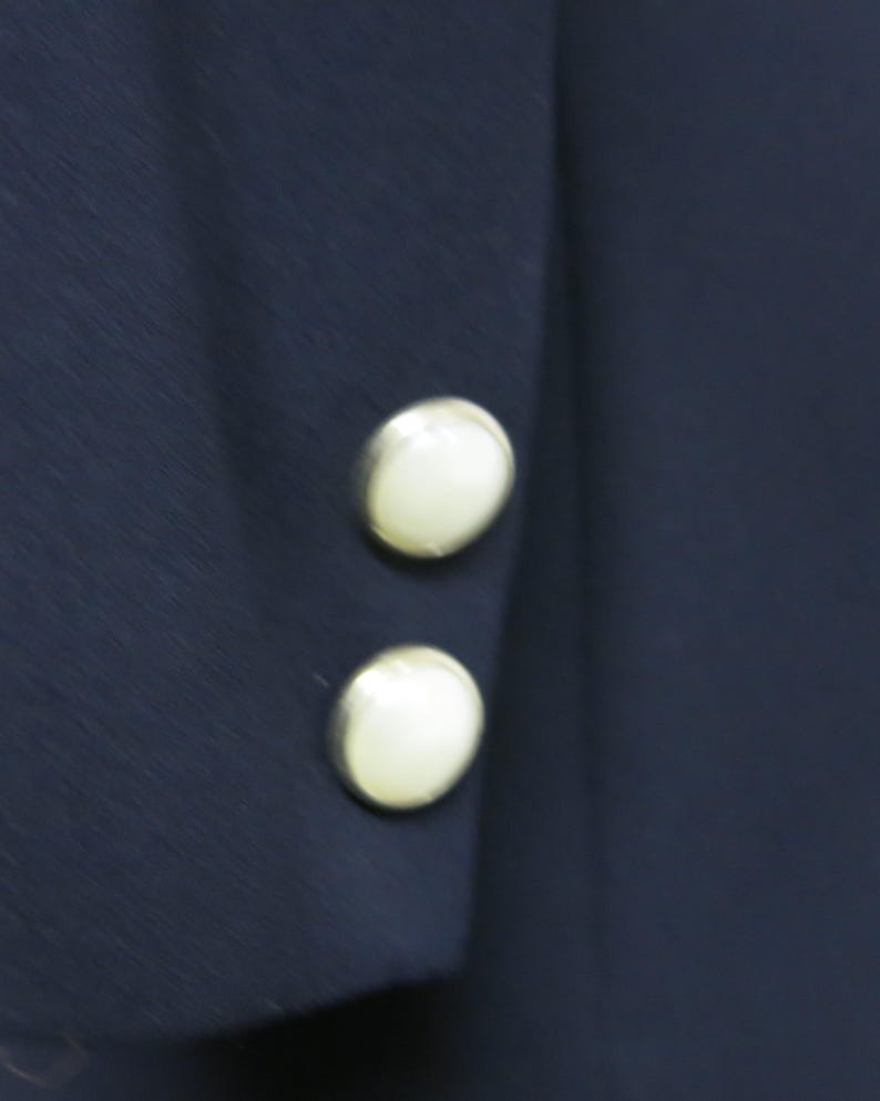 May include: Close-up of a navy blue jacket with two white pearl buttons on the sleeve.
