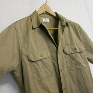 May include: A khaki short-sleeved work shirt with two chest pockets and a button-down collar.