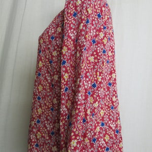 May include: A red long-sleeved blouse with a floral and star print. The blouse has a round neckline and long sleeves.