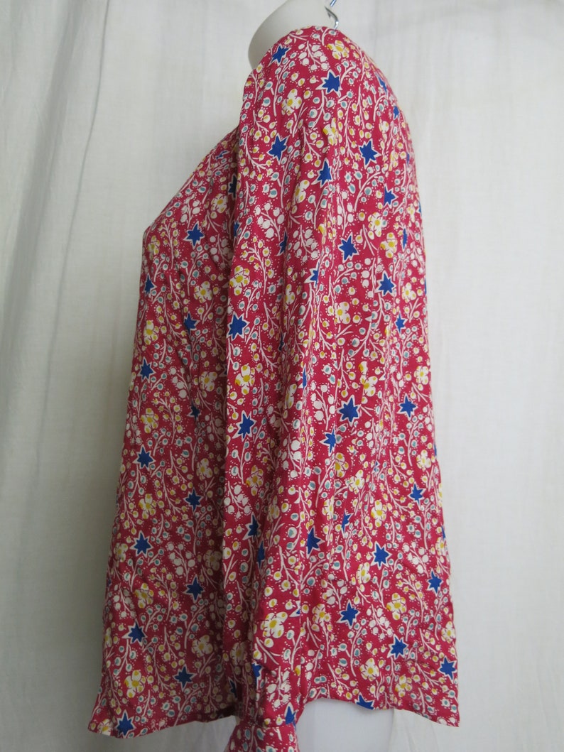 May include: A red long-sleeved blouse with a floral and star print. The blouse has a round neckline and long sleeves.