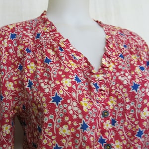 May include: A red, blue, and white floral print blouse with a ruffled neckline and button closure.