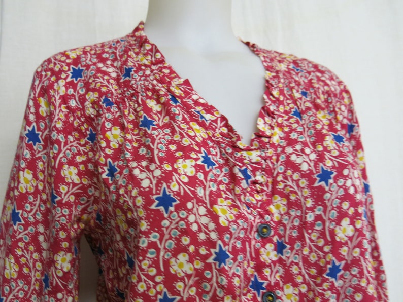 May include: A red, blue, and white floral print blouse with a ruffled neckline and button closure.