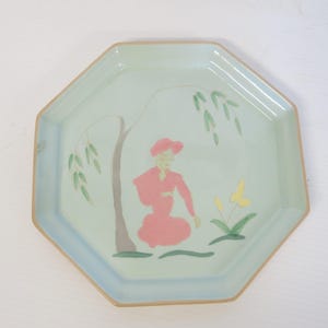 May include: Octagonal ceramic plate with a light blue background and a hand-painted design of a person in a pink dress standing under a willow tree with a yellow butterfly.