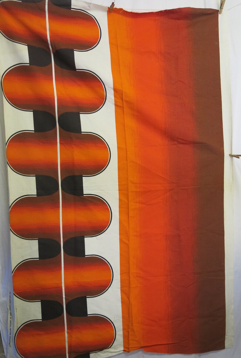 May include: Orange and brown fabric with a repeating pattern of rounded shapes. The fabric has a white background with a vertical line down the centre.