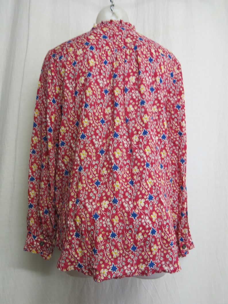 May include: A red, long-sleeved blouse with a floral print featuring blue stars and yellow flowers.