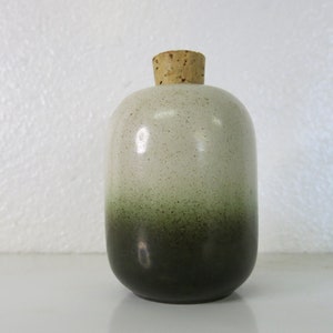 May include: A small, round ceramic bottle with a cork stopper. The bottle is white with a green ombre effect, fading to a dark green at the bottom.