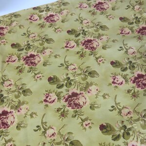 May include: A green fabric with a floral pattern featuring pink and burgundy roses. The fabric has a vintage look and feel.
