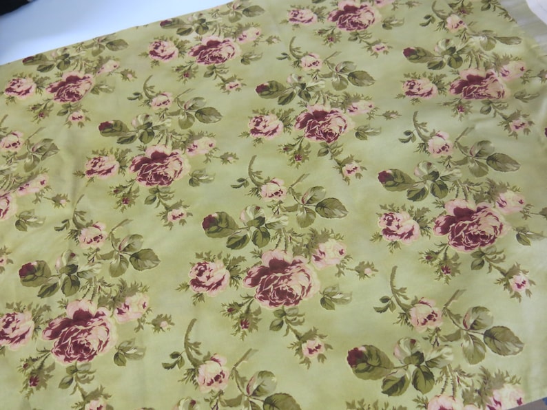 May include: A green fabric with a floral pattern featuring pink and burgundy roses. The fabric has a vintage look and feel.