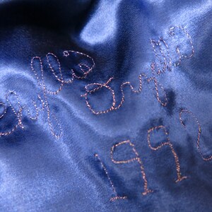 May include: Blue satin fabric with the words "We  Did It" embroidered in pink thread and the year "1992" embroidered below.