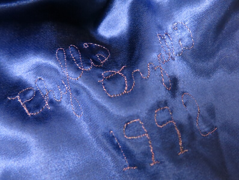 May include: Blue satin fabric with the words "We  Did It" embroidered in pink thread and the year "1992" embroidered below.