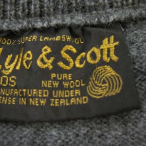 May include: A black label with gold text that reads "100% Super Lambswool Lyle & Scott XOS Pure New Wool Manufactured Under License in New Zealand". The label has a gold yarn ball graphic.