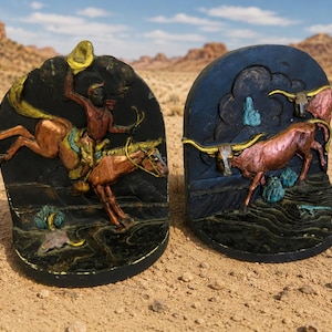 May include: Two decorative bookends with a Western theme. One features a cowboy on a horse, the other a longhorn. Both are black with colorful accents of brown, gold, and turquoise. The bookends are set against a desert backdrop.