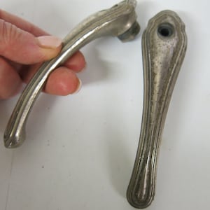 Może przedstawiać: Dwie vintage srebrne klamki do drzwi z ozdobnym wzorem. Klamki są w dobrym stanie z niewielkimi śladami zużycia.