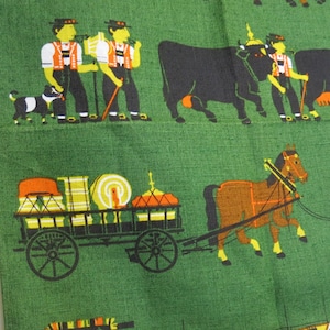 Op de afbeelding: Een groene stof met een herhalend patroon van mensen, dieren en een wagen. De mensen dragen traditionele kleding en dragen stokken. De dieren omvatten koeien, paarden en honden. De wagen is gevuld met verschillende items en wordt getrokken door een paard.