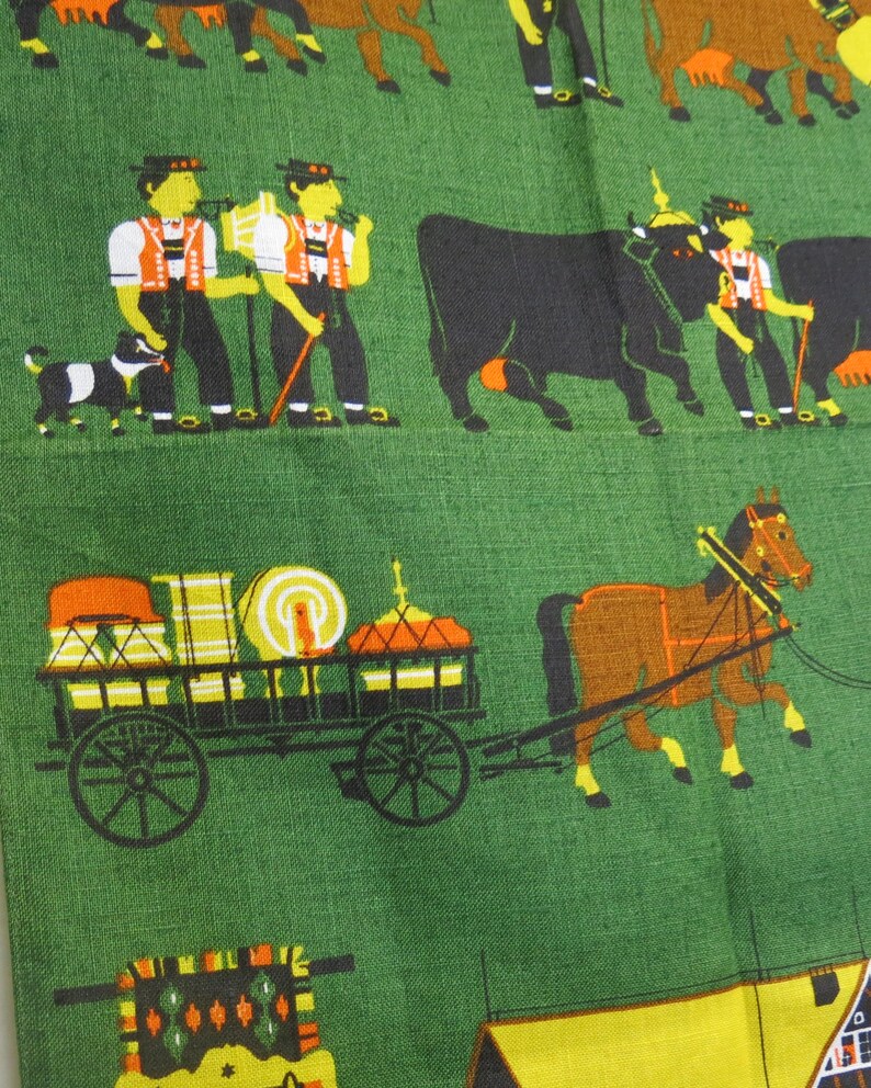 Op de afbeelding: Een groene stof met een herhalend patroon van mensen, dieren en een wagen. De mensen dragen traditionele kleding en dragen stokken. De dieren omvatten koeien, paarden en honden. De wagen is gevuld met verschillende items en wordt getrokken door een paard.