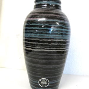 May include: A tall, ceramic vase with a dark, striped pattern in shades of black, blue, and gray. The vase has a rounded body and a narrow neck with a ridged rim. A circular sticker at the base reads "Made in USA, Harris Reserves, Chicago."