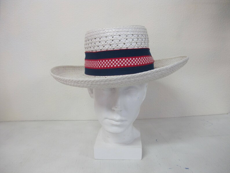 Puede incluir: Sombrero de paja blanco con una banda a cuadros azul y roja. El sombrero est&aacute; en una cabeza de maniqu&iacute; blanca.