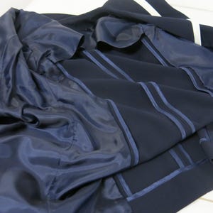 May include: A navy blue blazer with white stripes on the sleeves and a navy blue lining. The blazer is unbuttoned and the lining is visible.