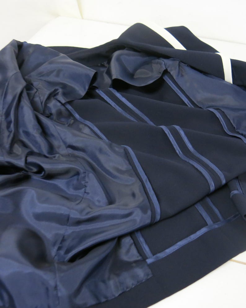 May include: A navy blue blazer with white stripes on the sleeves and a navy blue lining. The blazer is unbuttoned and the lining is visible.