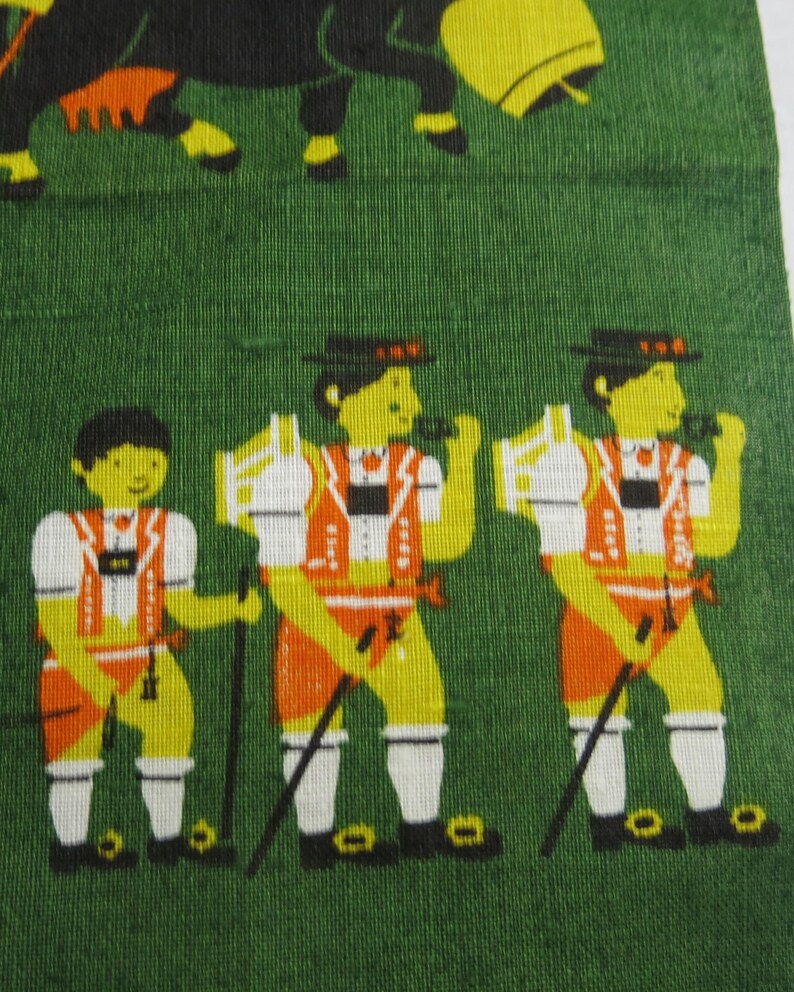 Op de afbeelding: Drie mannen in traditionele Beierse kleding staan op een groene achtergrond. Ze dragen groene hoeden, witte shirts, oranje vesten en oranje broeken. Ze houden wandelstokken vast.