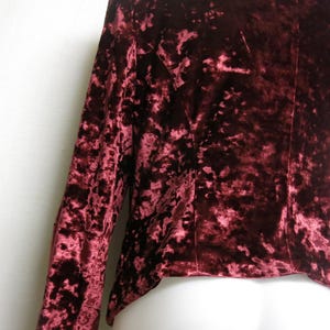 May include: A long-sleeved, burgundy crushed velvet top with a high neckline. The fabric has a textured, slightly raised pattern.
