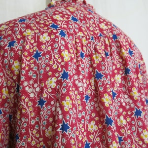 May include: A pink, blue, and white floral print shirt with a star pattern. The shirt has a ruffled collar and a gathered back.
