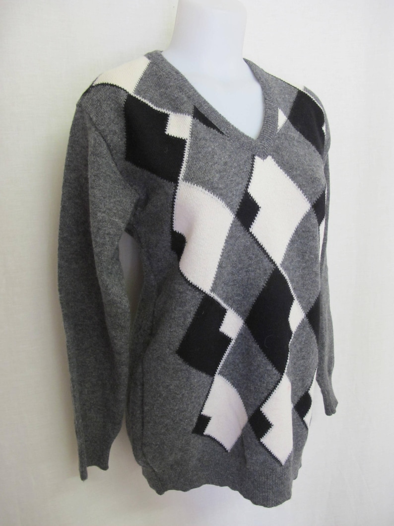 May include: A gray sweater with a black and white diamond pattern. The sweater has a v-neck and long sleeves.
