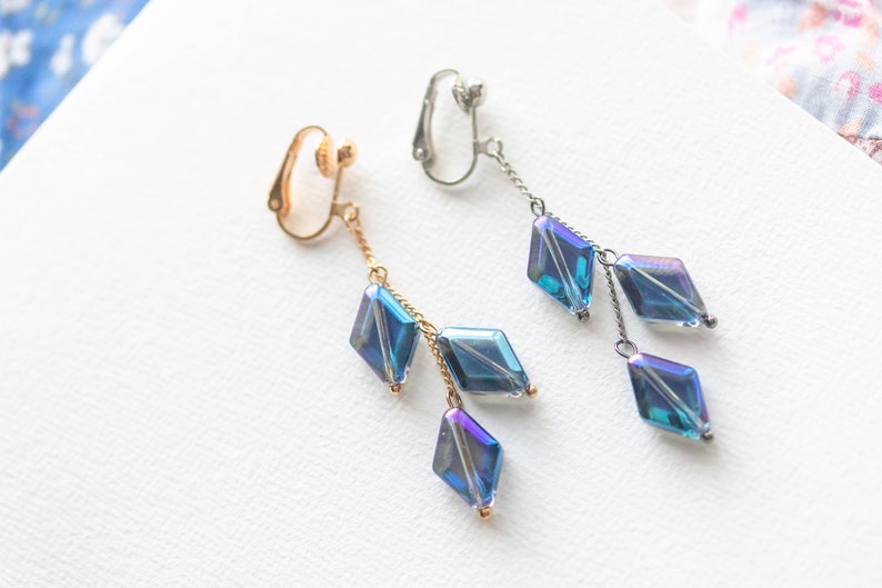 Peut inclure: Une paire de boucles d'oreilles &agrave; clip avec une cha&icirc;ne pendante et trois perles bleu iris&eacute; en forme de diamant.