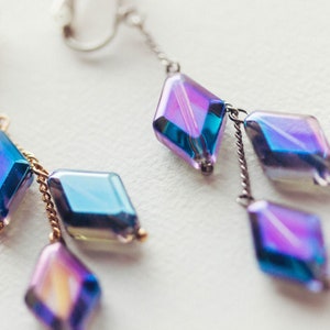 Peut inclure: Une paire de boucles d'oreilles pendantes avec des cristaux en forme de diamant bleu et violet iris&eacute;s suspendus &agrave; des cha&icirc;nes dor&eacute;es et argent&eacute;es.