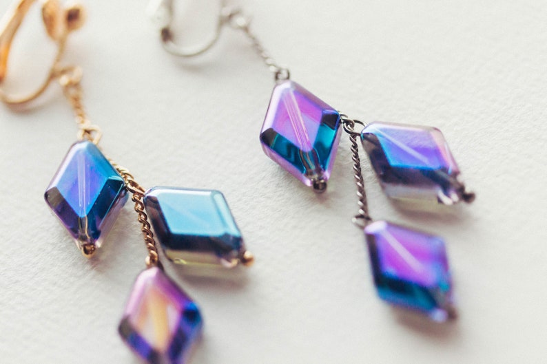 Peut inclure: Une paire de boucles d'oreilles pendantes avec des cristaux en forme de diamant bleu et violet iris&eacute;s suspendus &agrave; des cha&icirc;nes dor&eacute;es et argent&eacute;es.