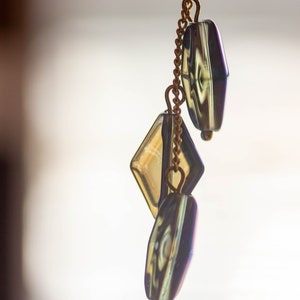 Peut inclure: Une cha&icirc;ne dor&eacute;e avec trois perles en verre iris&eacute;. Les perles sont en forme de diamant et de deux rectangles. La cha&icirc;ne est suspendue &agrave; un fond blanc.