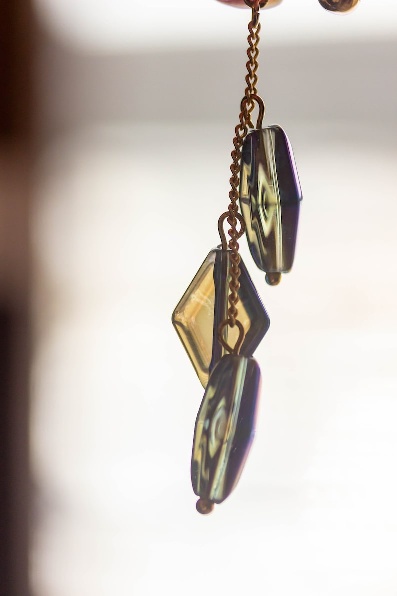 Peut inclure: Une cha&icirc;ne dor&eacute;e avec trois perles en verre iris&eacute;. Les perles sont en forme de diamant et de deux rectangles. La cha&icirc;ne est suspendue &agrave; un fond blanc.