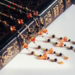 May include: Beaded bookmarks with orange, black, and brown beads are draped over a dark book with gold lettering. The bookmarks feature pumpkin-shaped beads. The book's title is "Moby Dick".
