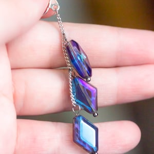 Peut inclure: Une paire de boucles d'oreilles pendantes en verre bleu et violet iridescent avec une fermeture &agrave; clip argent&eacute;e et une cha&icirc;ne.