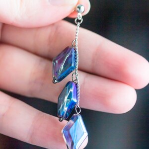 Peut inclure: Une boucle d'oreille en cha&icirc;ne argent&eacute;e avec trois perles de verre en forme de diamant bleu et violet iris&eacute;es.
