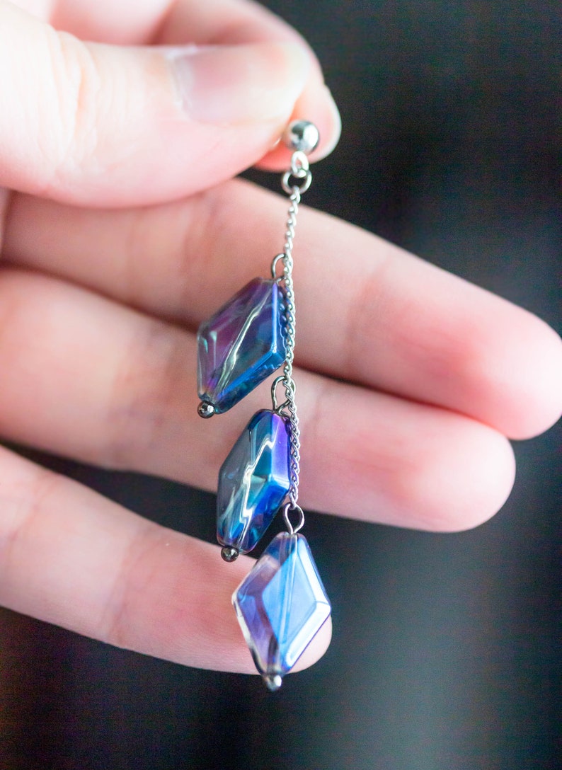 Peut inclure: Une boucle d'oreille en cha&icirc;ne argent&eacute;e avec trois perles de verre en forme de diamant bleu et violet iris&eacute;es.