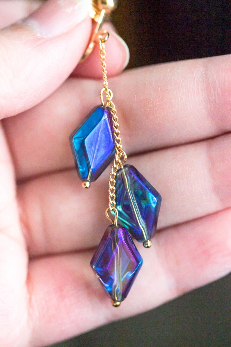 Peut inclure: Une cha&icirc;ne dor&eacute;e avec trois perles de verre en forme de diamant bleu et violet iris&eacute;.