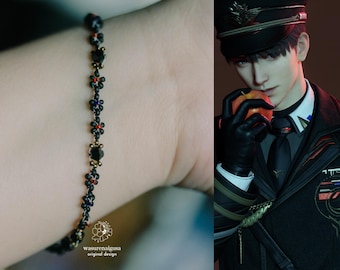 May include: A black beaded bracelet with small black, red, and blue flower accents. The bracelet is on a person's wrist. The text "wasurenaigusa original design" is at the bottom of the image.