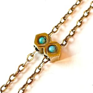May include: A gold-toned necklace with a double-sided pendant featuring two turquoise-colored stones. The pendant has a geometric design, and the chain is made of small, linked segments.