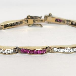 May include: A gold-toned bracelet with alternating sections of white and pink gemstones. The bracelet is secured with a clasp and is displayed against a white background. The gemstones are set in a curved design.