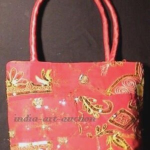 May include: A red handbag with two handles. The bag is decorated with gold and white floral embroidery and sequins. The text "india-art-auction" is visible on the front of the bag.