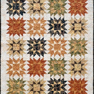 May include: A handmade quilt featuring a repeating star pattern in shades of brown, orange, green, and black. The stars are set against a white background with a quilted, wavy pattern. The quilt has a black border.
